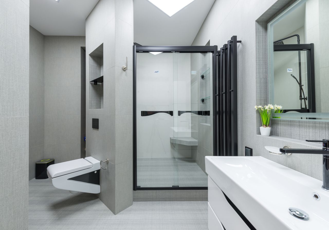 Sink with tap placed at wall with mirror in light spacious bathroom with toilet and glass shower cabin in apartment